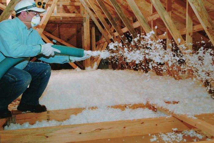 worker spraying insulation into attic